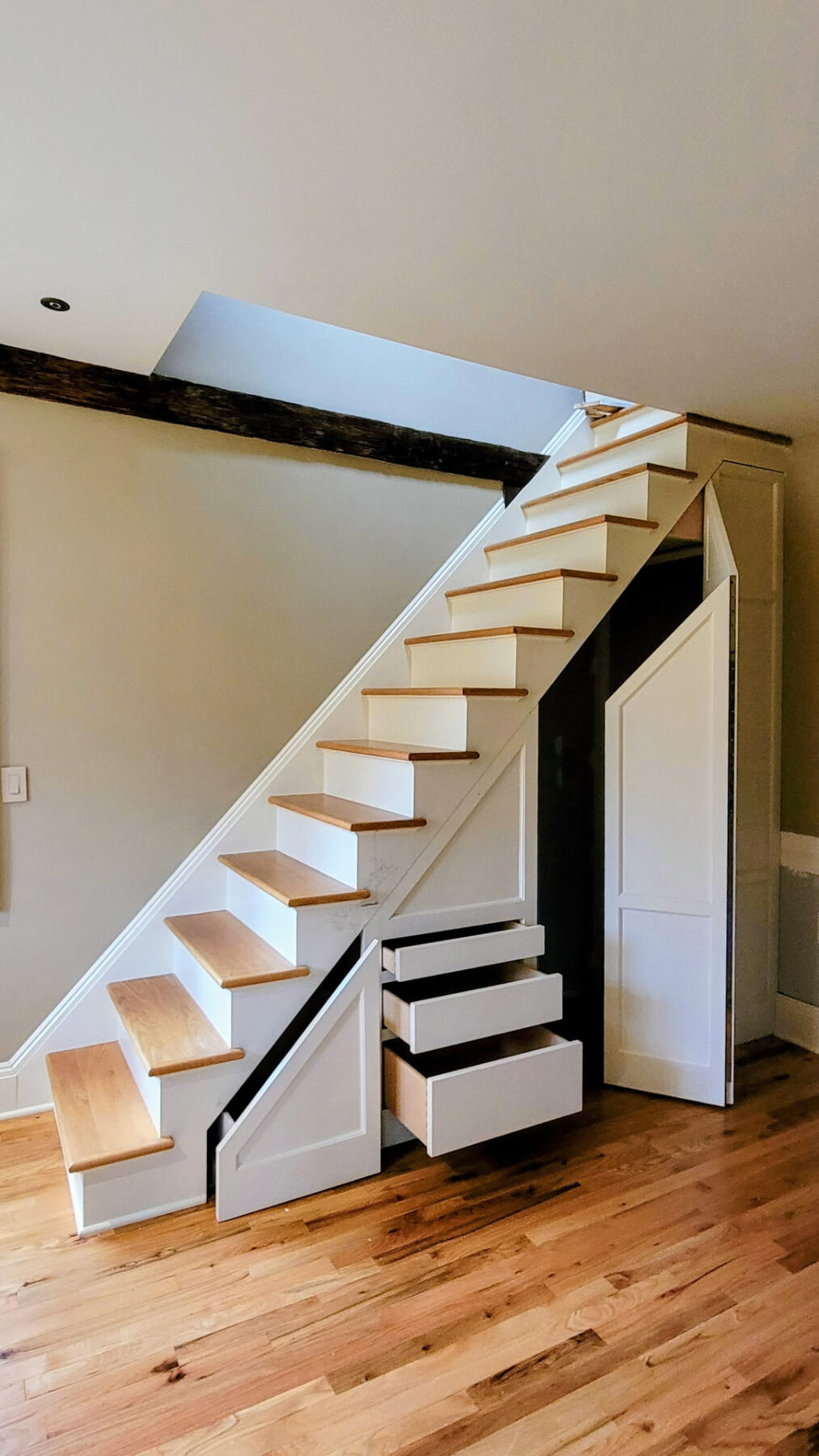 Custom under-stair storage with pull-out drawers and an open tall compartment revealing built-in storage
