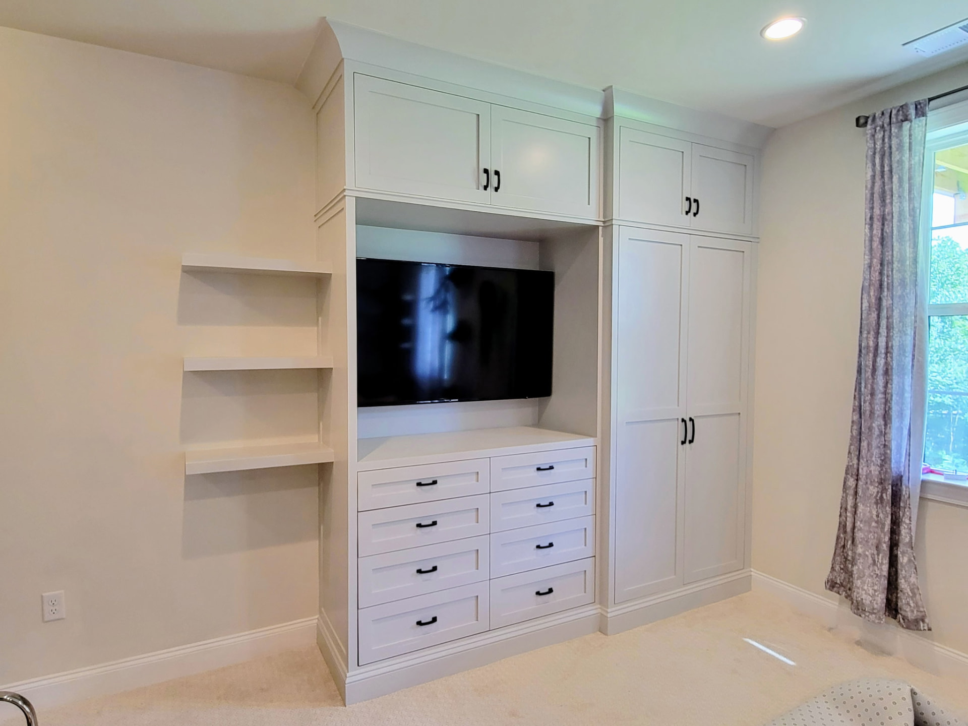 Custom bedroom built-in closet and TV cabinetry in Ridgefield CT by Glissmann Construction — finished white shaker-style cabinets with integrated drawers, open shelving and floor-to-ceiling storage